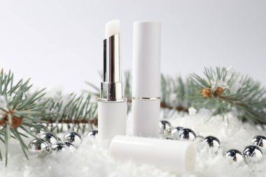 Nemlendirici dudak kremleri, Noel dekorasyonu ve beyaz arka planda suni kar üzerindeki köknar ağacı dalları, yakın plan. Kış bakımı