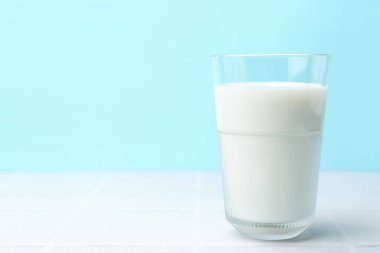 Açık mavi arka planda beyaz fayanslı masada bir bardak taze süt. Metin için boşluk