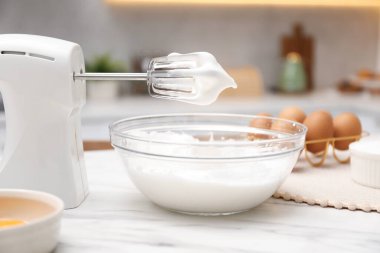 Çırpılmış çırpılmış çırpılmış krema ve yumurta dolu el çırpıcısı, mutfakta beyaz mermer masanın üzerinde.