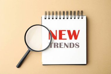 Not defterindeki yeni trendler ve bej arkaplan üzerindeki büyüteç, üst görünüm