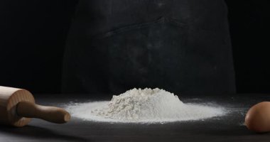 Siyah arkaplana karşı gri masada un yığınına yumurta eklemek, yakın plan. Para kazanmak.
