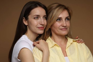 Açık kahverengi arka planda annesine sarılan bir kadın.