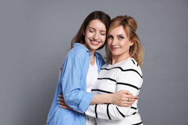 Anne ve kızı gri arka planda sarılıyorlar.