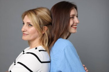 Neşeli anne ve kızı arka arkaya gri arka planda