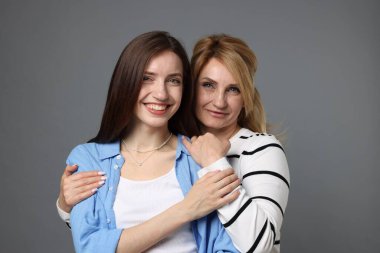 Anne ve kızı gri arka planda sarılıyorlar.