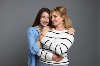 Anne ve kızı gri arka planda sarılıyorlar.