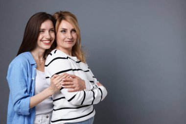 Anne ve kızı gri arka planda sarılıyorlar. Metin için boşluk