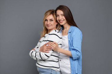 Anne ve kızı gri arka planda sarılıyorlar.