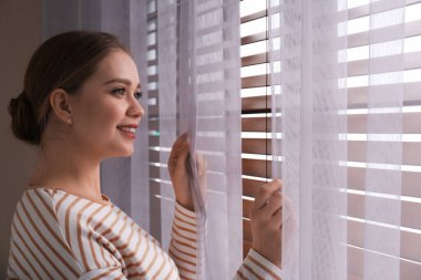 Woman near window with beautiful curtains at home