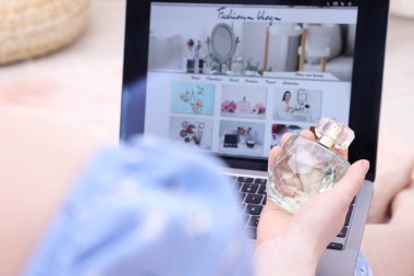 Blogcu dizüstü bilgisayarın yanında parfüm tutuyor moda blog sitesi kapalı, yakın plan