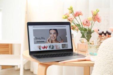 İçinde güzellik blogu olan dizüstü bilgisayar, çiçekler ve makyaj malzemeleri kapalı masa üzerinde.