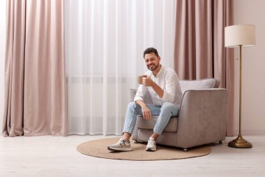 Gülümseyen adam evdeki güzel perdelerle pencerenin yanındaki koltukta dinlenirken çay içiyor. Metin için boşluk