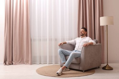 Evdeki güzel perdelerle pencerenin yanındaki koltukta dinlenen mutlu adam. Metin için boşluk
