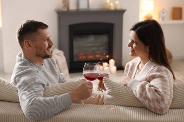 Şık şömineli koltukta kadeh tokuşturan mutlu çift.