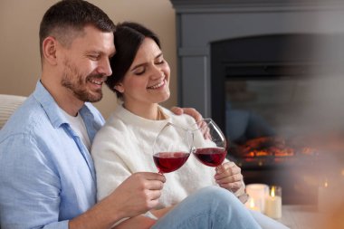 Mutlu çift evde şöminenin yanında kadeh tokuşturuyor.