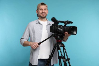 Açık mavi arka planda profesyonel video kamerası olan adam.