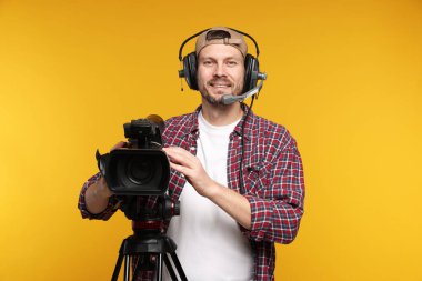 Profesyonel kamera ve turuncu arka planda kulaklığı olan bir adam.