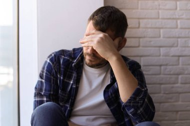 Evdeki pencerenin yanında oturan depresif bir adam.