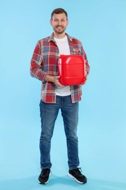 Açık mavi arka planda plastik kutu tutan adam.