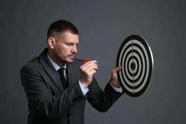 Hedef alınıyor. Dart tahtası ve gri arka planda oku olan bir adam.