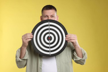 Hedef alınıyor. Sarı arka planda dart tahtası olan adam.