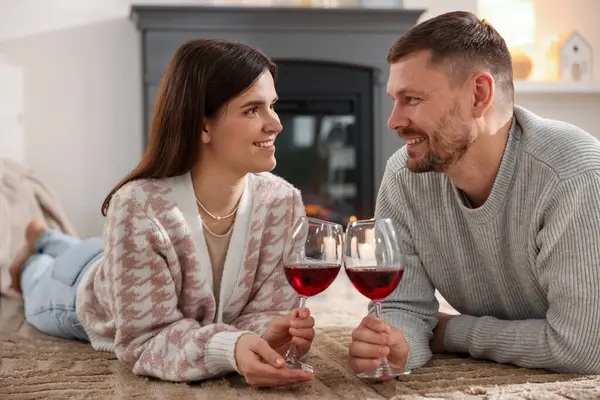 Evde şöminenin yanında şarap bardakları olan mutlu çift.