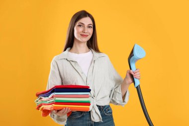 Buharlı bir kadın ve sarı arka planda bir yığın kıyafet.