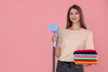 Buharlı bir kadın ve pembe arka planda bir yığın kıyafet. Metin için boşluk