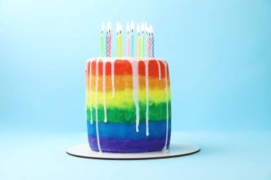 Açık mavi arkaplanda yanan mumlarla nefis gökkuşağı doğum günü pastası