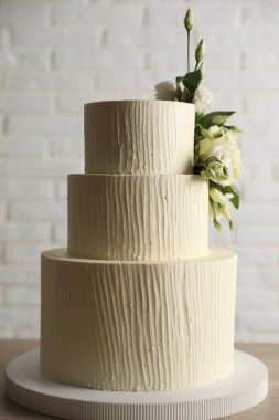 Beyaz tuğla duvarın yanındaki ahşap masada çiçeklerle süslenmiş nefis bir düğün pastası.