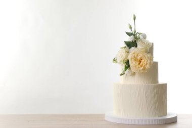 Ahşap masadaki çiçeklerle süslenmiş nefis düğün pastası beyaz arka planda. Metin için boşluk