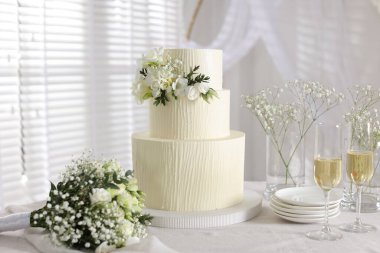 Çiçek desenli nefis düğün pastası, çiçek buketi ve kapalı bir masada bir bardak şampanya.