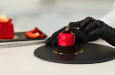 Mutfaktaki beyaz ahşap masada lezzetli bir tatlıyı dekore eden şekerci, yakın plan.