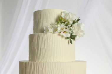 Çiçekli nefis düğün pastası ve beyaz arka planda perdeler, yakın plan.