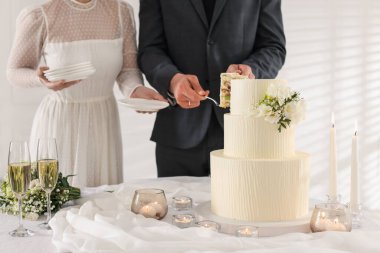 Damat düğün pastasından bir parça alırken gelin tabakları içeride tutuyor, yakın plan.