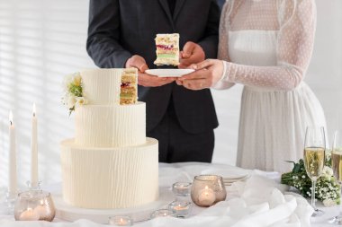 Damat, düğün pastasından bir parça tabağa koyuyor. Gelini masada kapalı tutuyor, yakın plan.