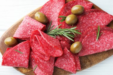 Beyaz ahşap masada servis edilen zeytinli ve biberiyeli lezzetli sosis dilimleri.