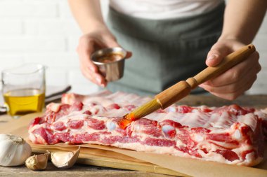 Kadın, masadaki çiğ domuz pirzolasına terbiye koyuyor.