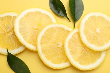 Sarı arka planda taze limon ve yeşil yapraklar var.