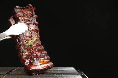 Siyah arka planda ızgaradan maşayla leziz domuz pirzolası alıp yakın plan çekiyoruz. Metin için boşluk