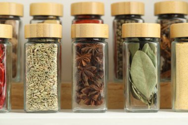 Beyaz masadaki kavanozlardaki farklı aromatik baharatlar, yakın plan.