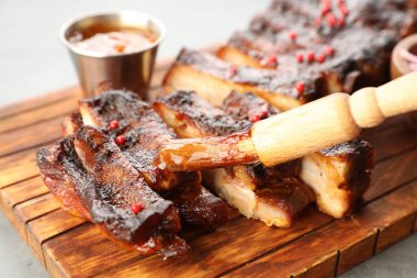 Gri masadaki leziz domuz kaburgalarının üzerine fırçayla sos serpiştiriyorum.