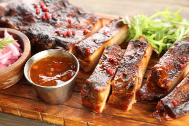 Lezzetli domuz pirzolası, roka, sos ve soğan ahşap masada, yakın plan.