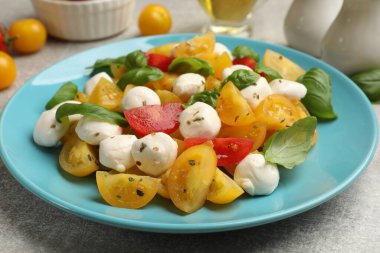 Sarı domatesli lezzetli salata, fesleğen ve mozzarella peyniri açık gri masada, yakın plan.