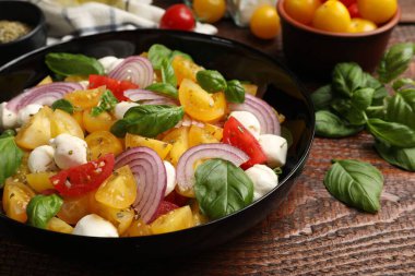 Sarı domatesli lezzetli salata, fesleğen, soğan ve ahşap masada mozzarella peyniri, yakın plan.