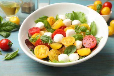 Sarı domatesli lezzetli salata, fesleğen ve mozzarella peyniri açık mavi ahşap masada, yakın plan.