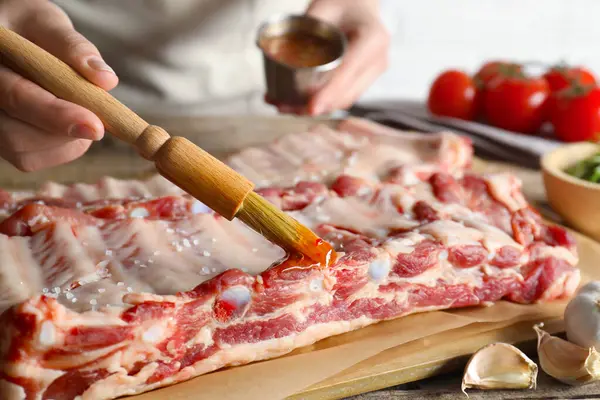 Kadın, masadaki çiğ domuz pirzolasına terbiye koyuyor.