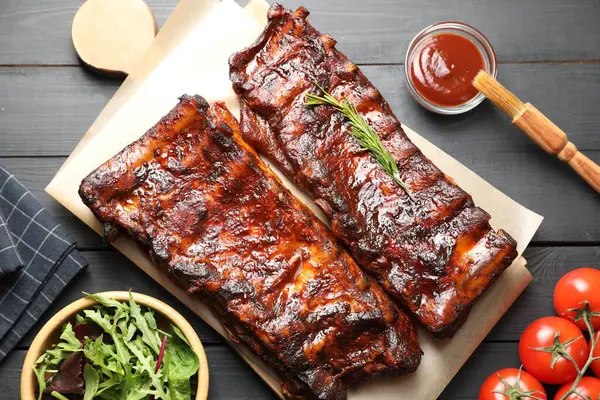 Biberiye, domates, sos ve salata ile servis edilen kızarmış domuz kaburgaları siyah ahşap masada, düz yatıyordu.