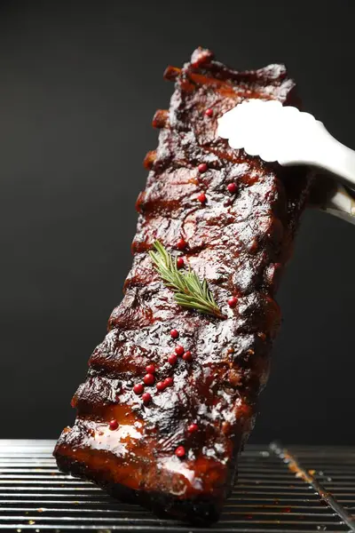 Siyah arka planda ızgaradan maşayla leziz domuz pirzolası alıp yakın plan çekiyoruz.