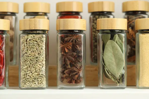 Beyaz masadaki kavanozlardaki farklı aromatik baharatlar, yakın plan.